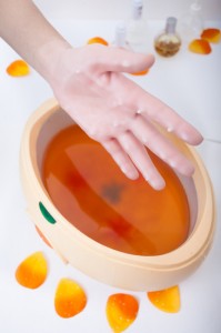 Female hand orange parrafin wax in bowl. Manicure beauty spa salon